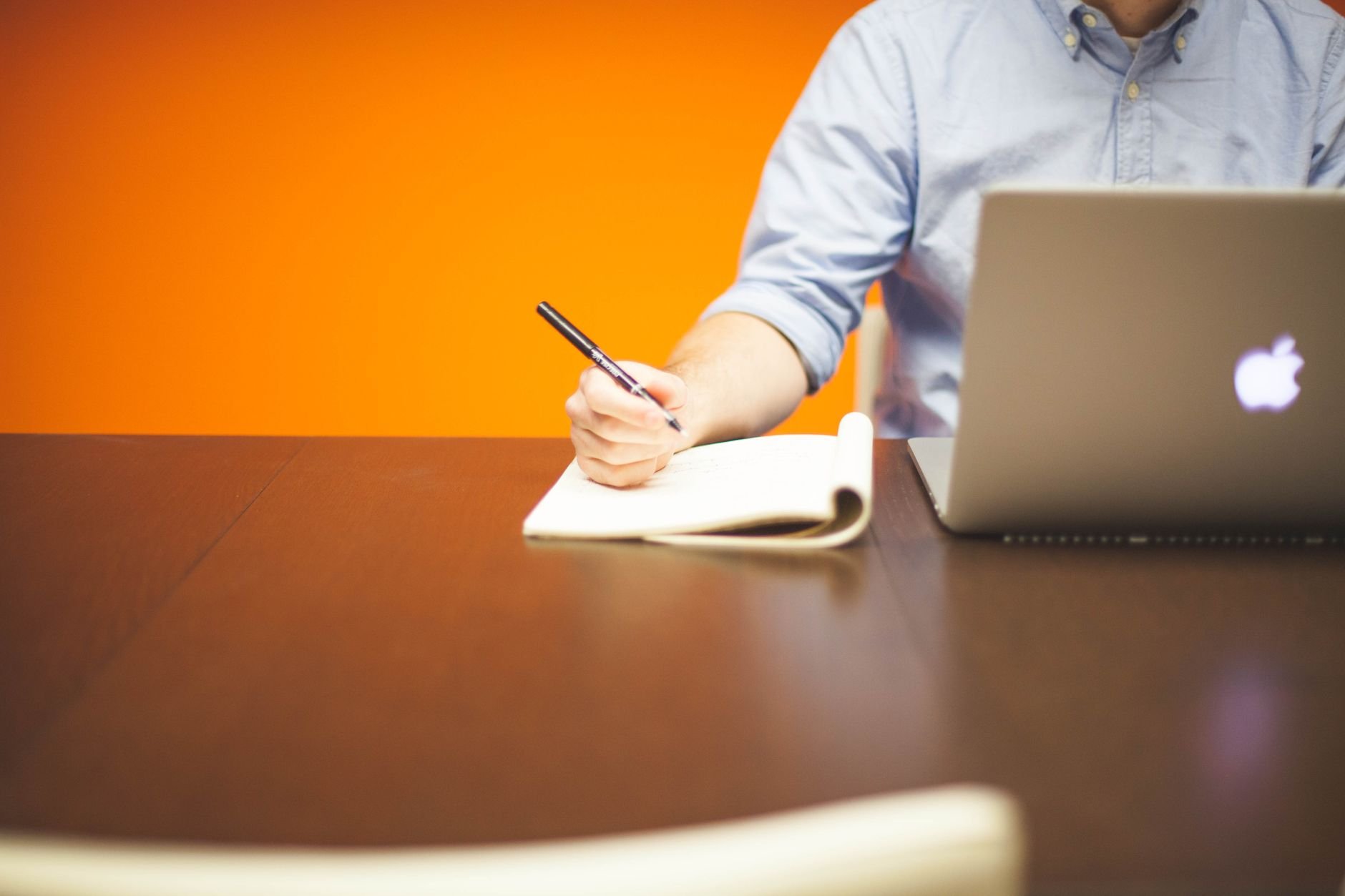 Founder writing notes in notebook beside laptop, working on business idea